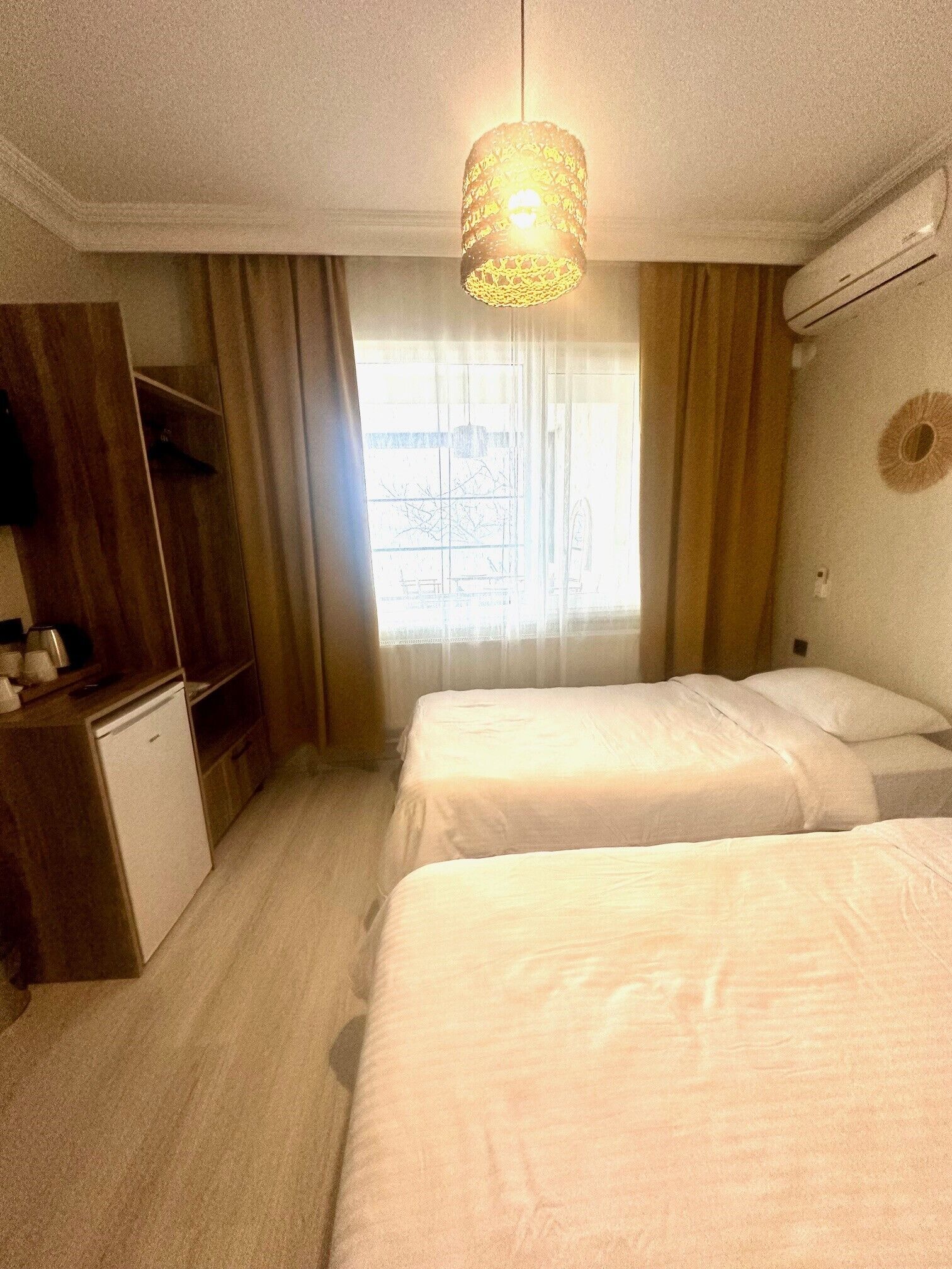 Une chambre d’hôtel avec deux lits, un bureau, un petit réfrigérateur, une fenêtre avec des rideaux et un appareil de climatisation fixé au mur.