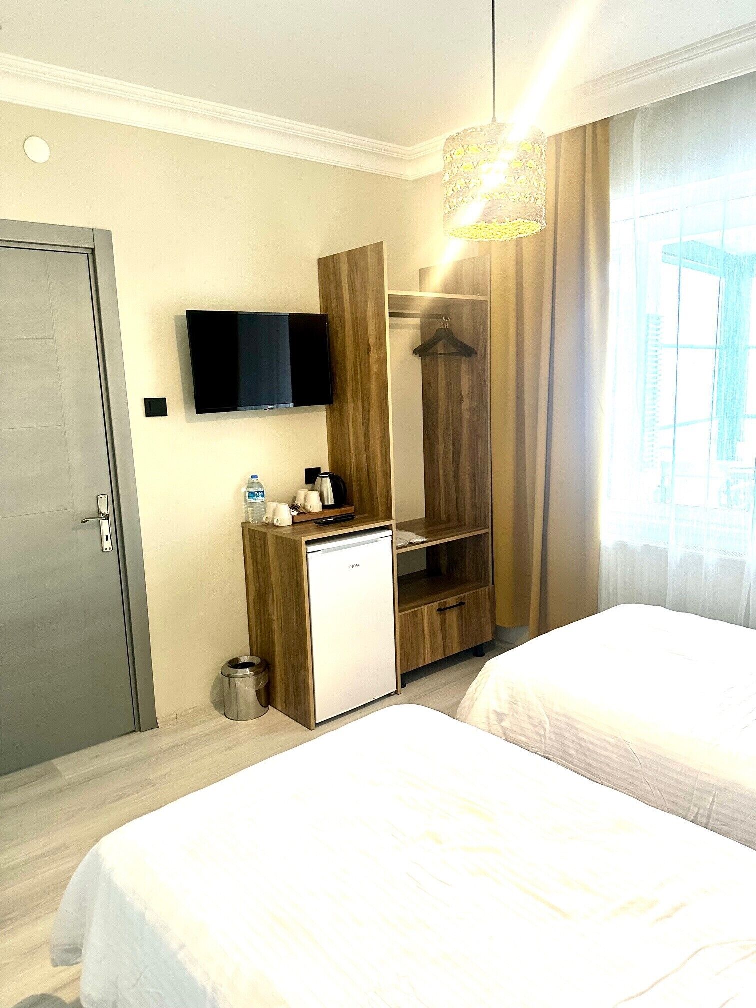 A hotel room with two beds, a minibar, a television, a wardrobe, and a window with curtains.