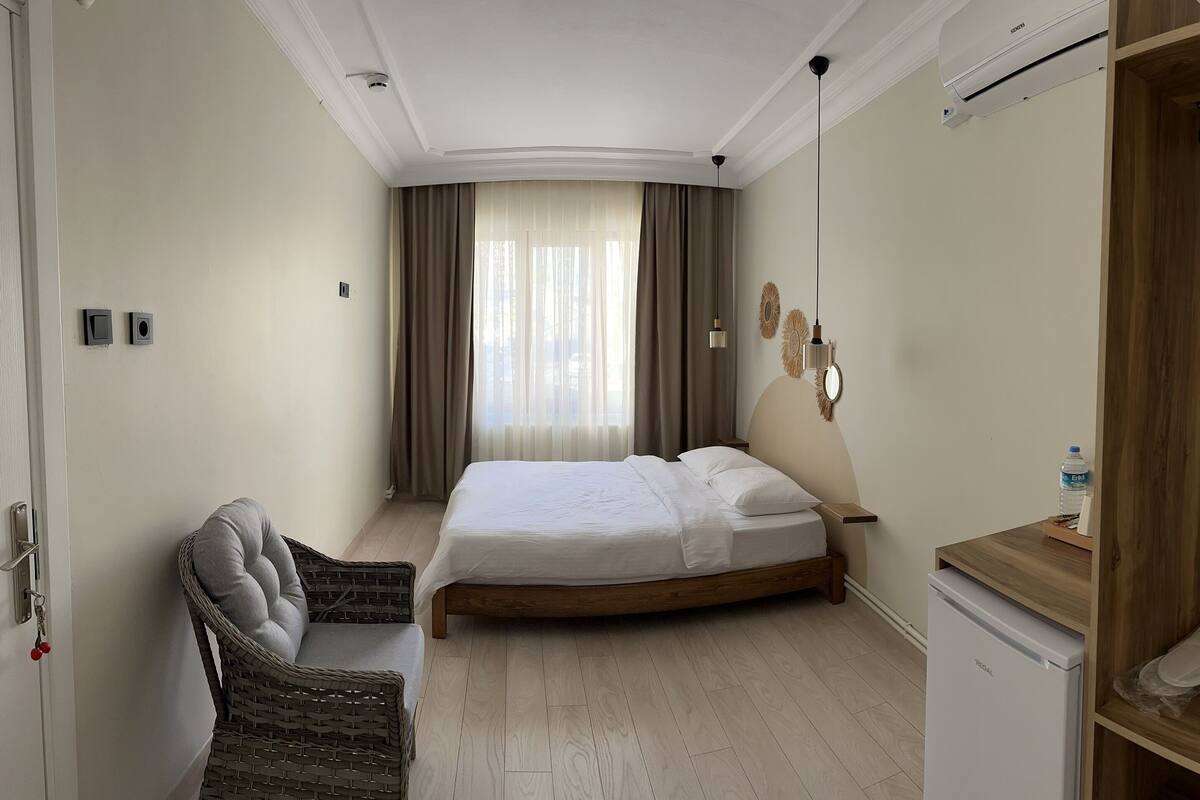 A hotel room with a bed, a chair, a small table, a wardrobe, and a wall-mounted air conditioner.