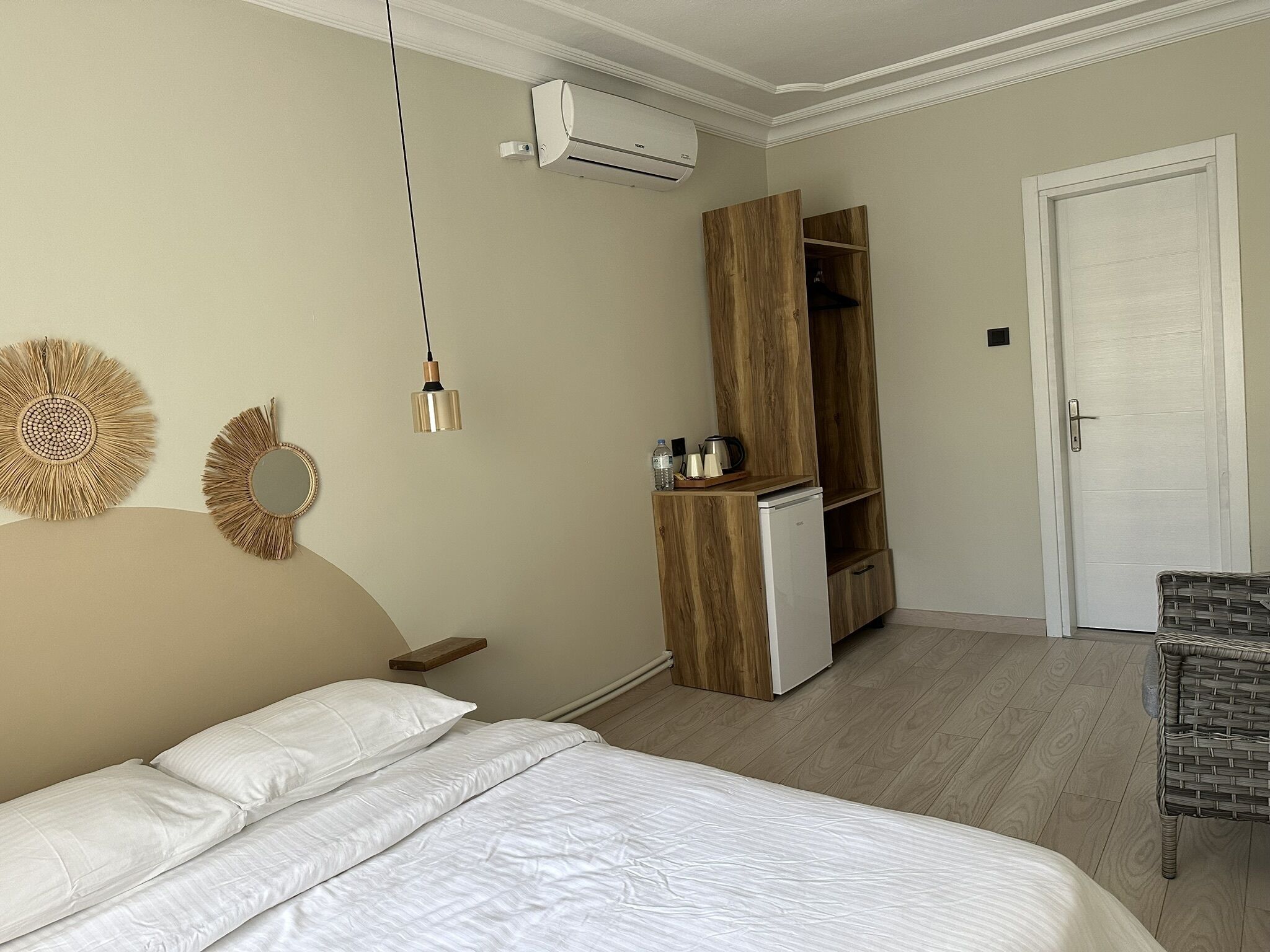 Une chambre avec un lit, une armoire, un petit réfrigérateur, une lampe suspendue et une porte.