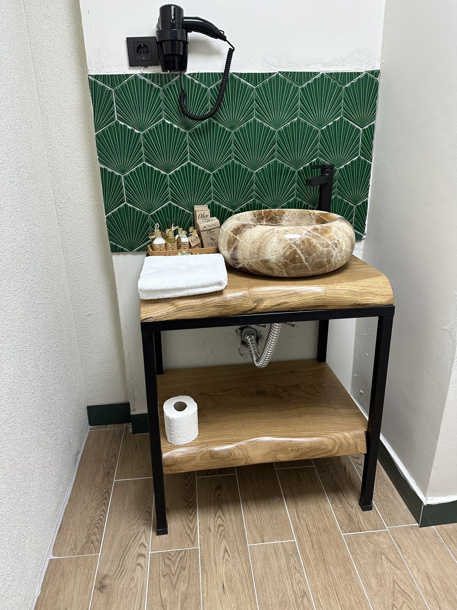 A bathroom with a wooden vanity, a green patterned tile backsplash, and a sink with a stone basin.