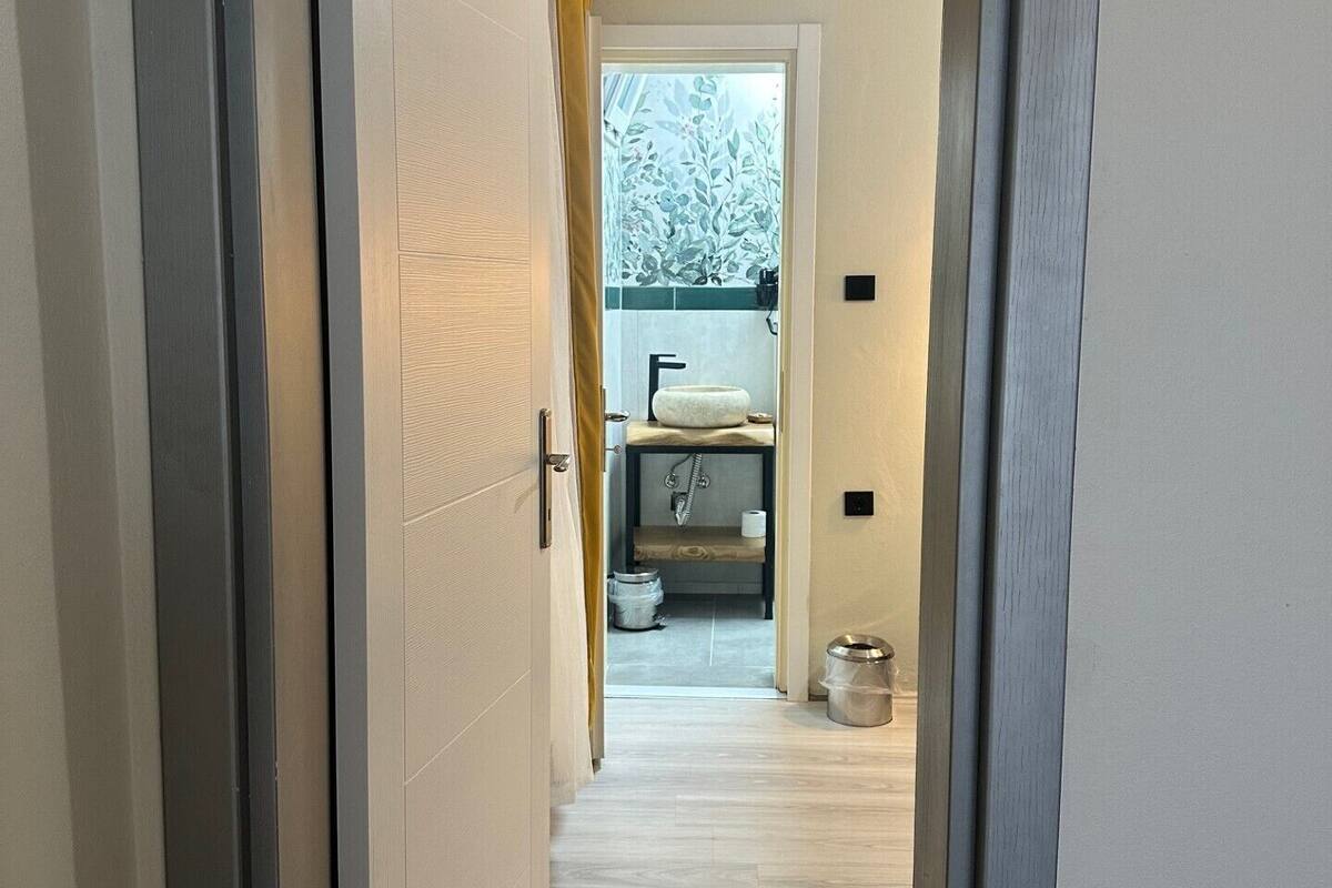 A hallway with a door leading to a bathroom. The bathroom has a toilet, sink, and a window.