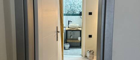 Un pasillo con una puerta que da a un baño. El baño tiene un inodoro, un lavabo y una ventana.