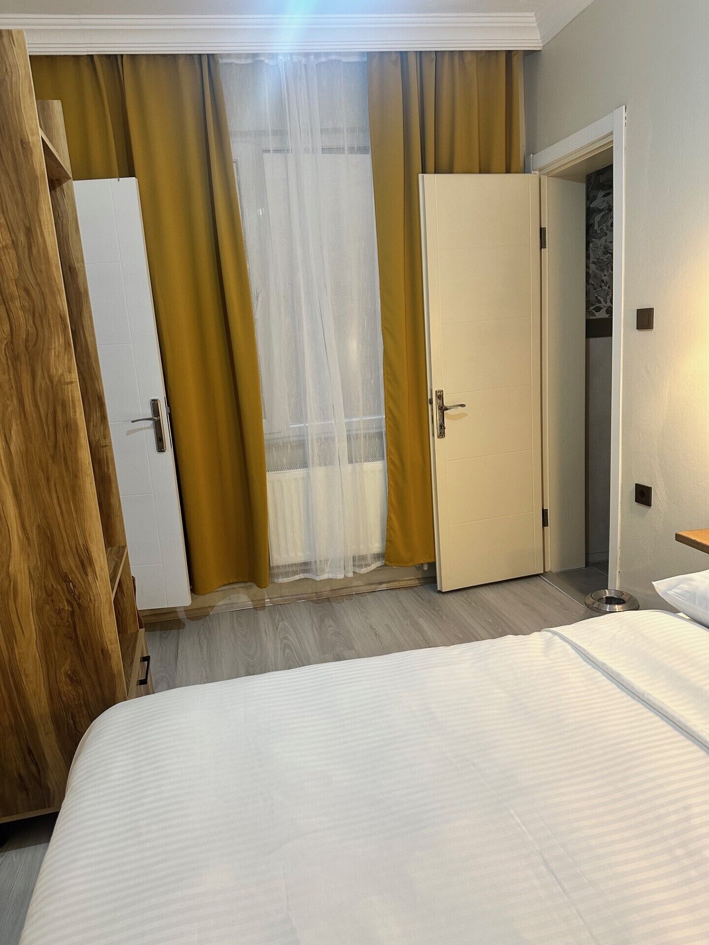 A hotel room with a bed, a wardrobe, a door, and a window with curtains.