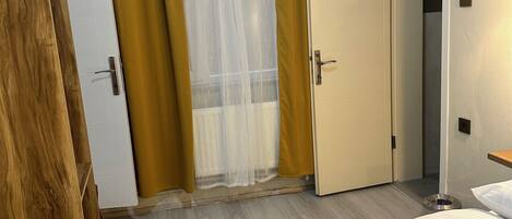Una habitación de hotel con cama, armario, puerta y ventana con cortinas.