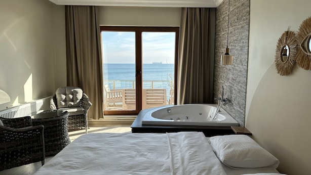 A hotel room with a large bed, a bathroom with a bathtub, a wicker chair, a view of the sea, and a balcony. - Kingway Suite (Tekirdag)