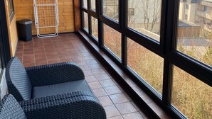 En balkong med utsikt över byggnader och träd, ett metallställ och en svart soffa.