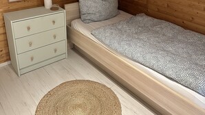 Ett sovrum med ett träpanelat tak, en säng med mönstrat sänglinne, ett nattduksbord med lådor, en inramad tavla och en dekorativ girlang av trianglar.