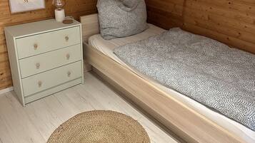 Ein Schlafzimmer mit Holzboden, einem Bett mit gemusterten Betttextilien, einem Nachttisch mit Schubladen, einem gerahmten Bild und einer dekorativen Kette aus Dreiecken.