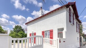 Een wit gebouw met rode luiken en een witte poort.