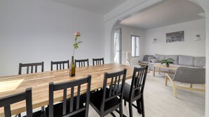 Een eetgedeelte met een houten tafel en zwarte stoelen, een vaas met een bloem, en een grijze bank op de achtergrond.