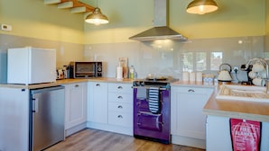 Une cuisine moderne avec des meubles blancs, un four violet, un four à micro-ondes et un réfrigérateur.