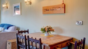 Un coin repas avec une table en bois, des chaises, un vase de fleurs, des lampes fixées au mur et une enseigne indiquant « The Walnut ».