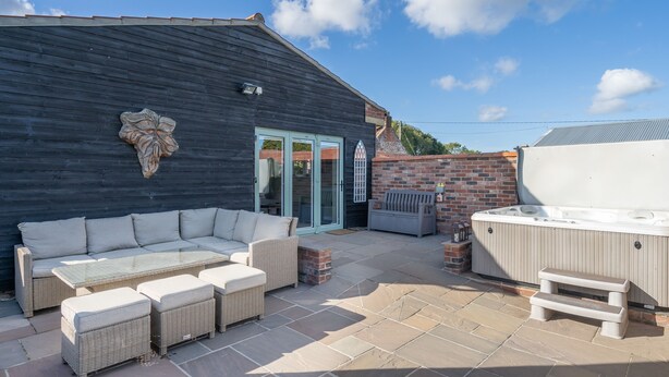 Une terrasse extérieure aménagée avec un canapé, des poufs, une table à plateau en verre et un jacuzzi.