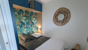 A bedroom with a bed, a wall-mounted mirror, and a tropical-themed wallpaper.