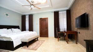Una habitación de hotel con cama, escritorio, silla, televisión y ventilador de techo.