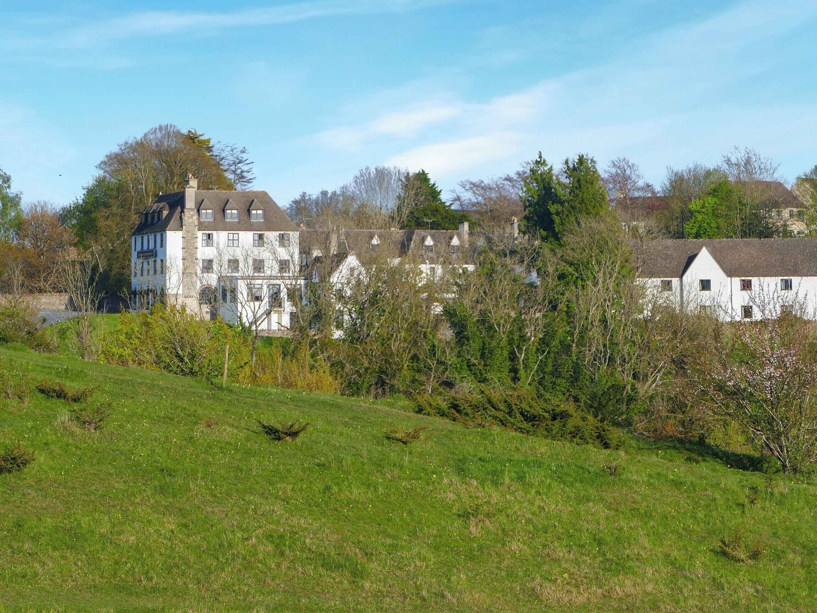 A large white building with multiple windows and a sloped roof, surrounded by greenery and trees.