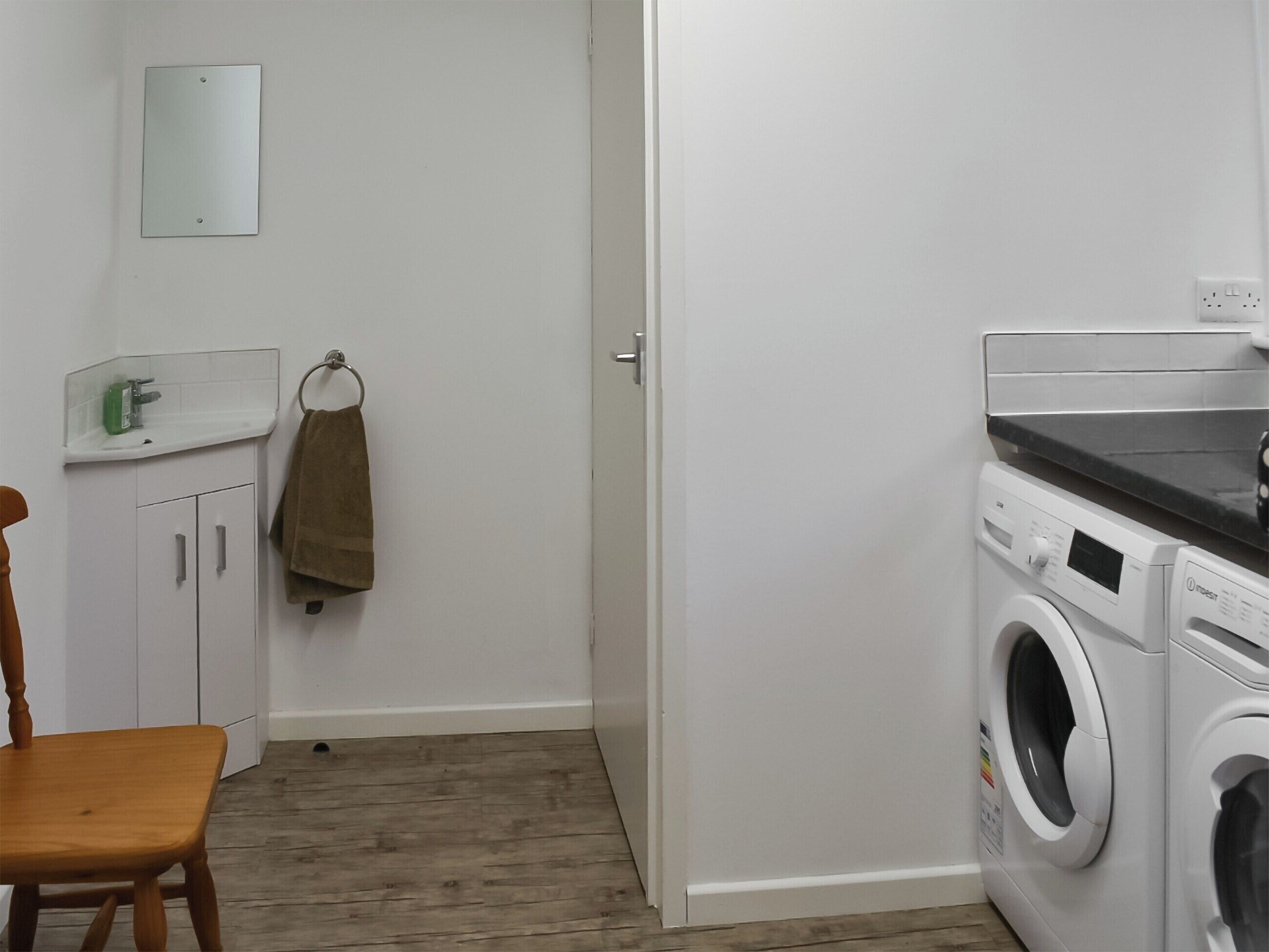 A laundry room with a washing machine, a sink, and a mirror on the wall.