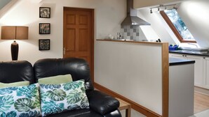 A modern kitchen with a skylight, a dining area with a black leather sofa, and a wooden door. - A cosy one-bedroom first floor apartment on Rodborough Common. (Rodborough Common, near Stroud)