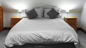 A neatly made bed with white bedding and two gray pillows, flanked by wooden nightstands with lamps. - A cosy one-bedroom first floor apartment on Rodborough Common. (Rodborough Common, near Stroud)