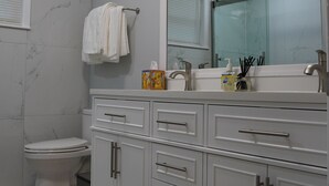 A bathroom with a white vanity, a large mirror, a toilet, and a shower area. - Spacious Home with Luxury Finish (Brandon)