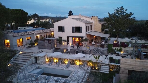 Ein mehrstöckiges Haus mit Terrasse, Sitzgelegenheiten im Freien und einem Schwimmbecken.