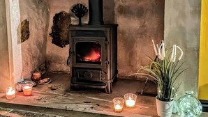 A rustic room with a wood-burning stove, candles, and a potted plant. - Mynydd A Mor, Mountains and Sea (Trefor, near Caernarfon)