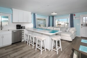 Una cocina moderna con armarios blancos, una isla central con taburetes, una cafetera y vistas al exterior.