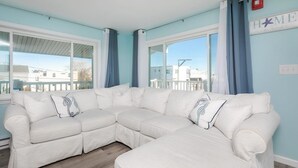 A white sectional sofa with decorative pillows in a room with light blue walls and large windows. - Short stroll to the beach! Newly renovated, 3 bedroom condo, wrap around porch (Hampton)