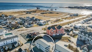 An aerial view of a coastal town with residential buildings, a large pink building, and a beach in the background. - Short stroll to the beach! Newly renovated, 3 bedroom condo, wrap around porch (Hampton)