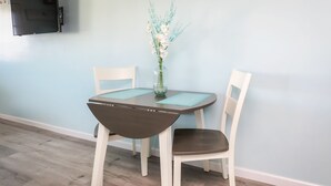 A dining area with a table and two chairs, a vase with flowers, and a flat-screen TV mounted on the wall. - Short stroll to the beach! Newly renovated, 3 bedroom condo, wrap around porch (Hampton)