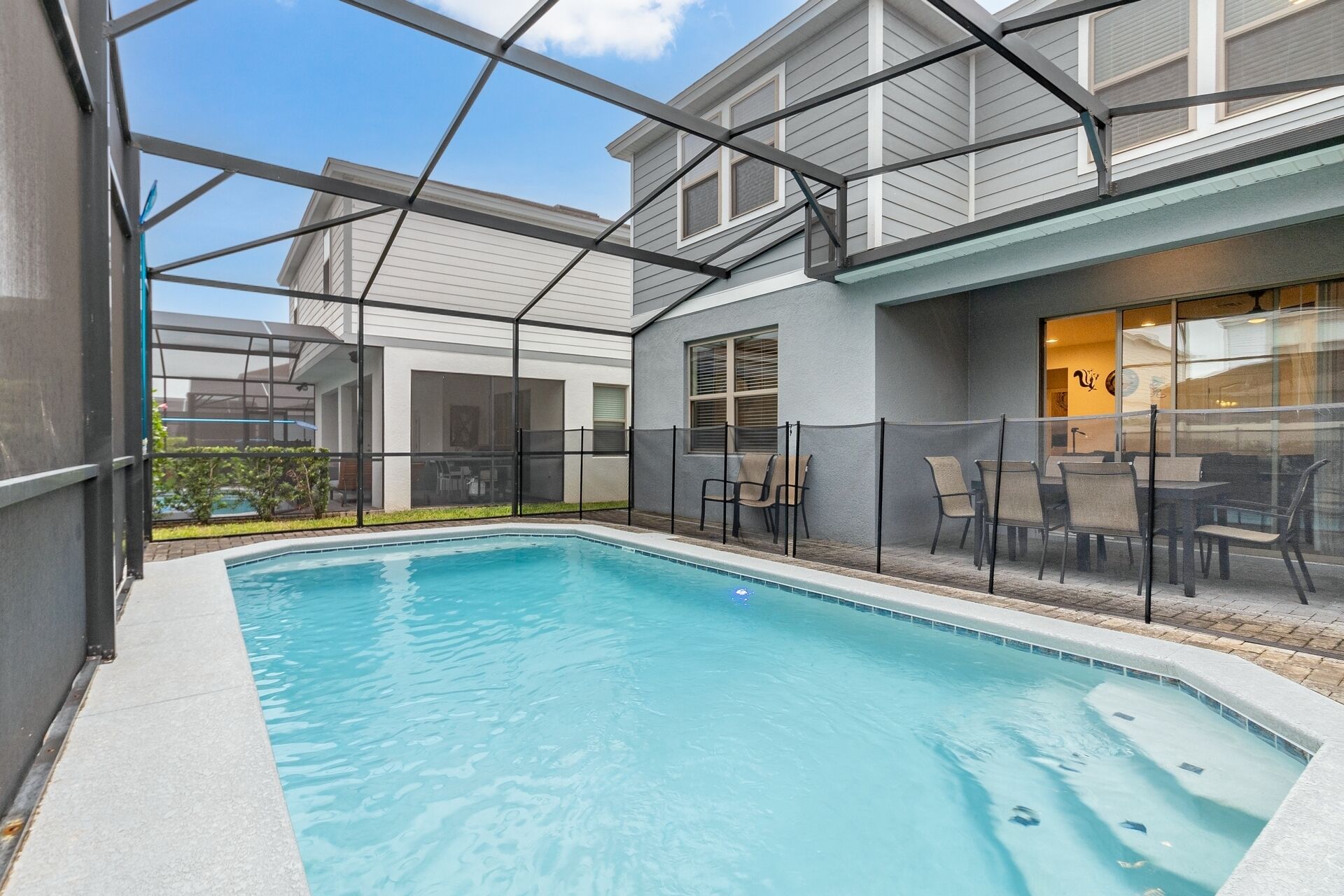 Ein Schwimmbad mit Glasveranda, Sitzgelegenheiten im Freien und ein Gebäude mit großen Fenstern.