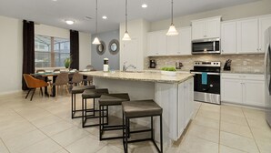 A modern kitchen with white cabinets, stainless steel appliances, and a central island with bar stools. - Disney Emerald in Windsor Westside-Stunning 5 bed villa close to all attractions (Four Corners)