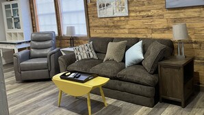 Un salon moderne avec un mur en bois, un canapé gris, une table basse jaune et un fauteuil gris.