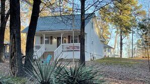 Une maison blanche avec un porche, entourée d’arbres et d’une pelouse.