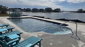 Ein Pool mit einer Metallleiter, umgeben von türkisfarbenen Stühlen und Tischen, mit Blick auf Häuser über dem Wasser.