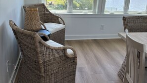 Ein Zimmer mit Korbmöbeln, Blick auf ein Gewässer und ein Fenster mit Jalousien.