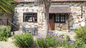 A stone house with a wooden door, two windows, and a small garden with purple flowers. - 1 bedroom accommodation in Brighstone (Brighstone)