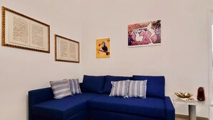 A modern living room with a blue sectional sofa, striped pillows, framed artwork on the wall, and a small side table with a red object. - Donna Rebecca, apartment in fine building with garden (Meta)