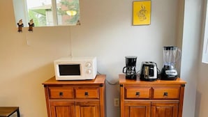 Et kompakt køkken med en mikrobølgeovn på et træskab, en kaffemaskine og en blender på et andet skab.