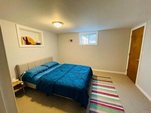 A bedroom with a bed, a small window, a door, and a wall-mounted artwork. - Spacious, stocked 1 BR Suite with Yard in Edmonds! (Edmonds)