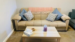 En beige sofa med mønstrede puder, et træbord med en servietæske og et lys, og en grøn sofa i baggrunden.