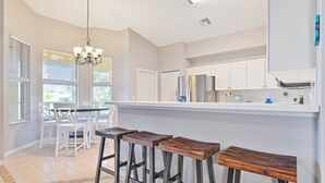 A modern kitchen with white cabinets, a stainless steel refrigerator, and a bar area with wooden stools. - 3/2.5 lakefront condo with 2-car garage in gated community, close to beaches  (Fort Myers)