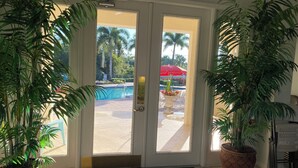 A hotel entrance with a glass door leading to a pool area, surrounded by potted plants. - 3/2.5 lakefront condo with 2-car garage in gated community, close to beaches  (Fort Myers)