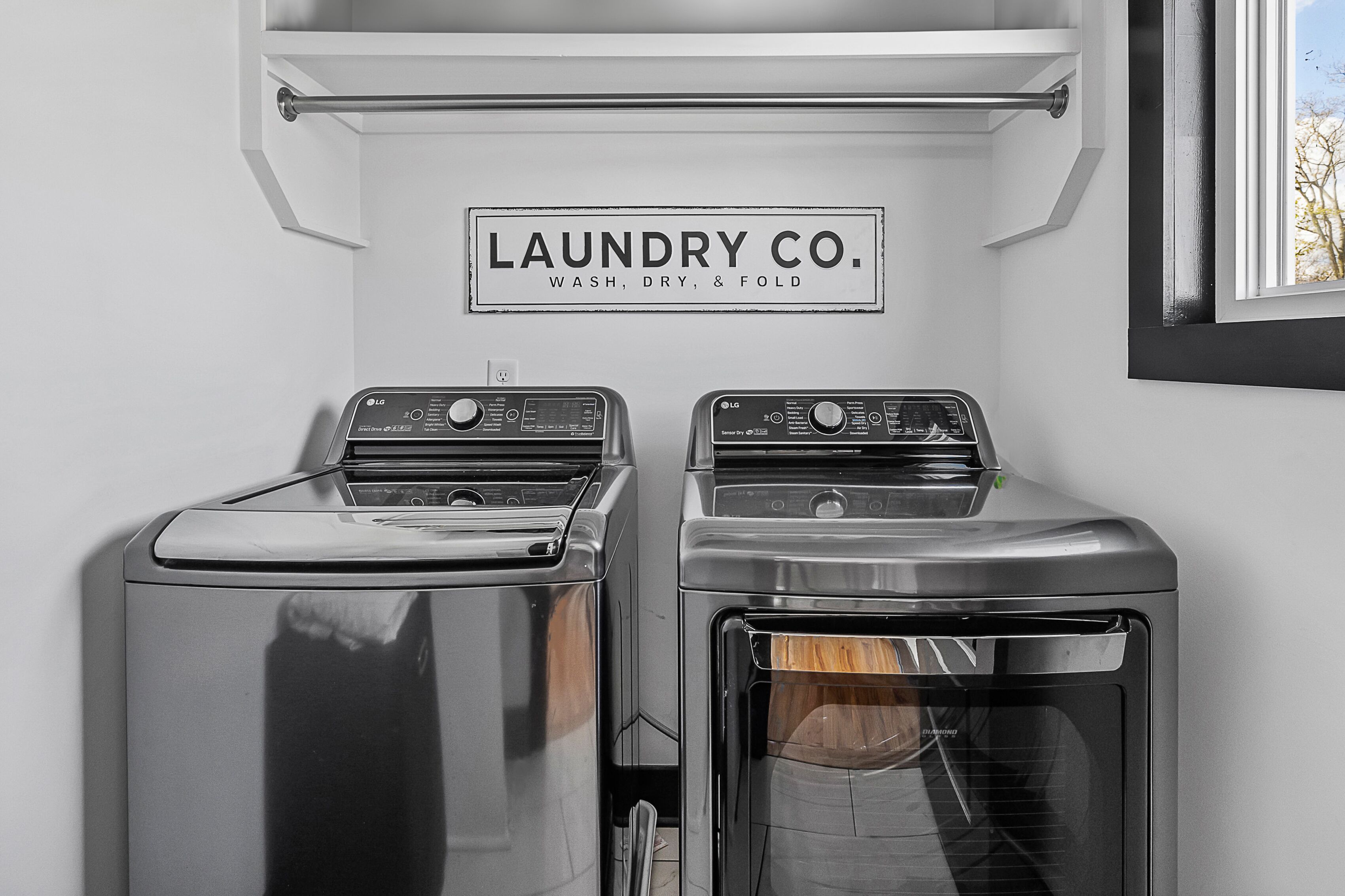 A laundry area with two washers and a dryer, a sign above them, and a window to the right.
