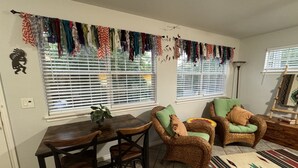 A dining area with a wooden table and chairs, a woven chair with cushions, a patterned rug, and a wall-mounted drying rack with clothes. - Native Sun - Free Boat/Trailer parking (Medicine Park)