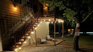 A covered outdoor seating area with a staircase leading to a building, surrounded by gravel and a tree. - Native Sun - Free Boat/Trailer parking (Medicine Park)