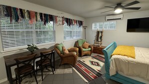 A room with a bed, a desk, two chairs, a floor lamp, and a wall-mounted TV. - Native Sun - Free Boat/Trailer parking (Medicine Park)