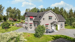 A two-story house with a red awning, a porch with outdoor furniture, and a well-maintained lawn.