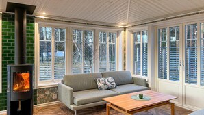 A cozy room with a fireplace, a sofa, a coffee table, and large windows offering a view of the outdoors.